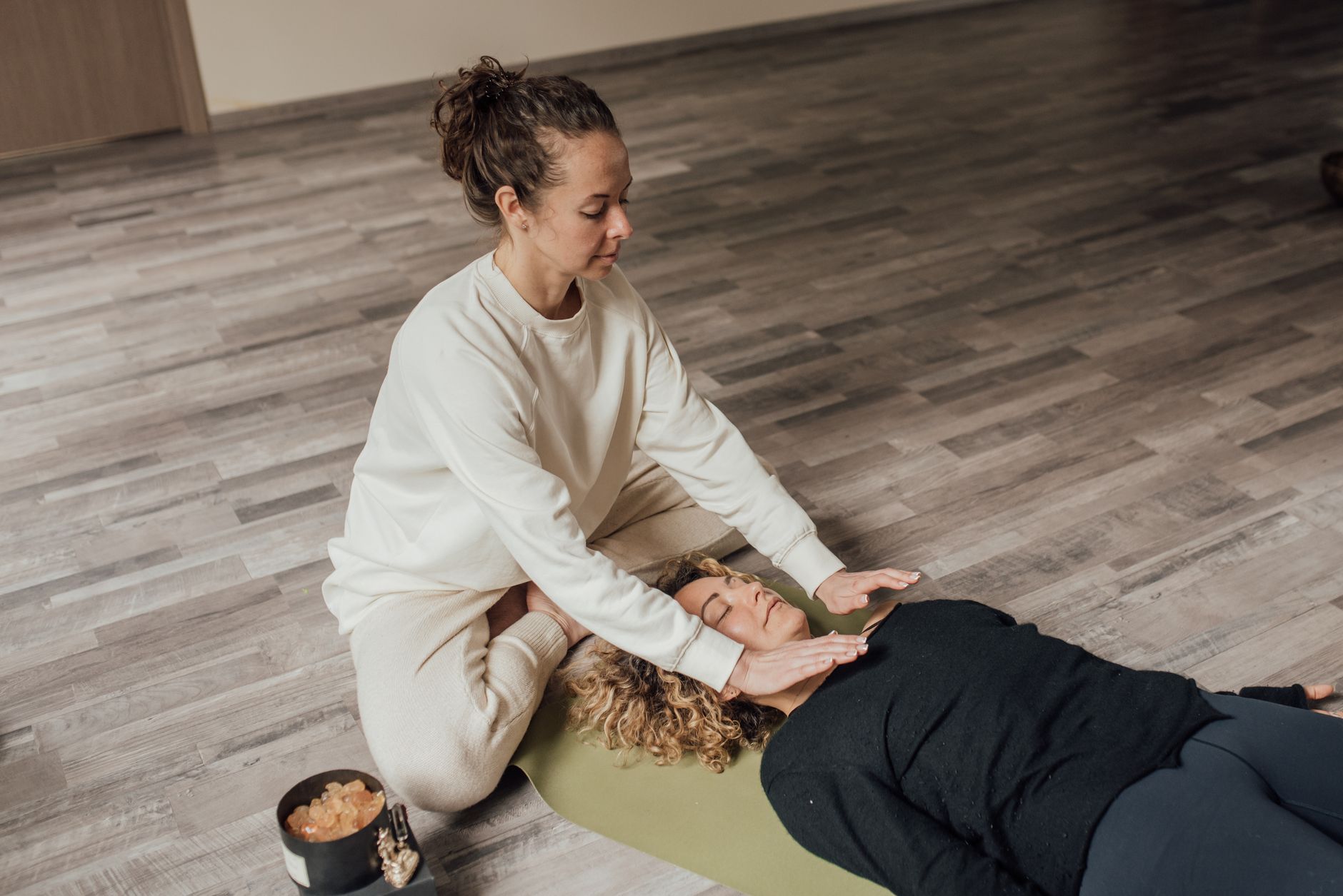 Kobieta wykonuje terapię Reiki na osobie leżącej na macie do jogi